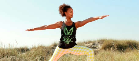Eine Frau macht eine Yoga Übung am Strand auf einer Düne.