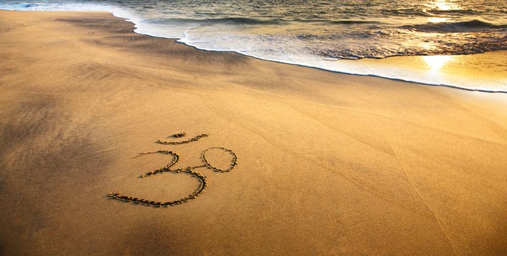 Ein Yoga Symbol ist an einem Strand in den Sand gemalt worden.