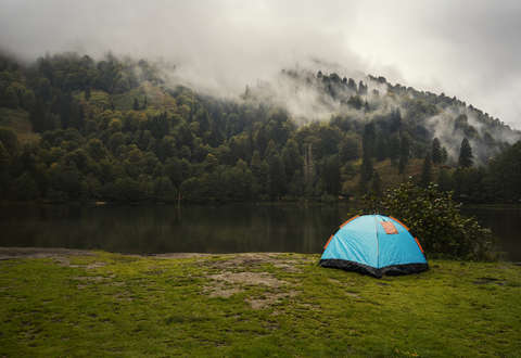 Ein Zelt steht bei regnerischem Wetter an einem Seeufer.