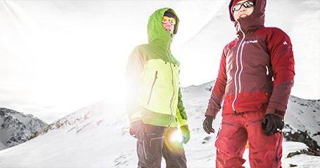 Zwei Personen in Funktionsklamotten und Sonnenbrillen stehen in einer winterlichen Landschaft