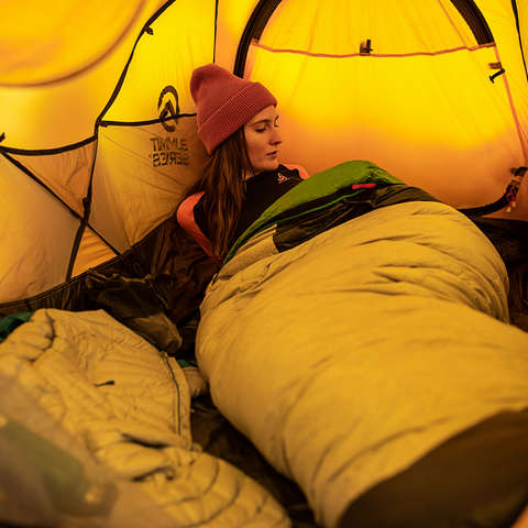 Eine Frau liegt im Zelt in einem warmen Schlafsack