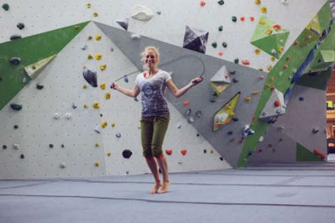 Eine Frau wärmt sich mit Seilspringen in einer Boulderhalle auf. Bild 1