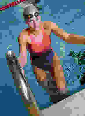 Eine Frau in einem sportlichen Badeanzug steigt aus einem Schwimmbecken.