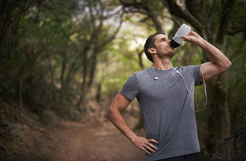 Ein Läufer steht im Wald und trinkt aus einer weißen Trinkflasche.