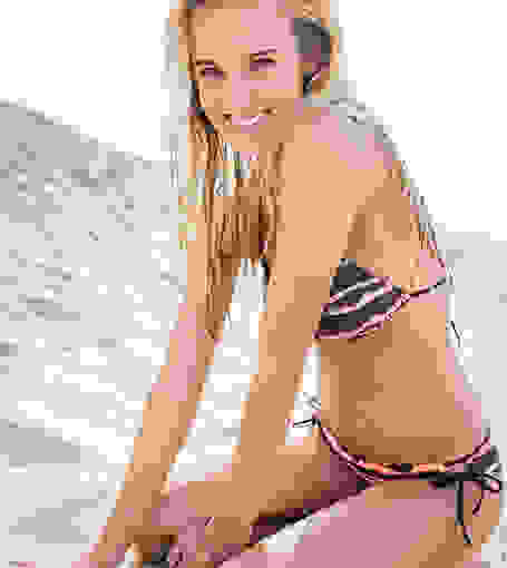 Eine Frau kniet im Bikini an einem weißen Sandstrand.