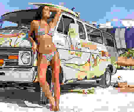 Eine Frau lehnt in einem bunten Bikini an einem Multivan, der mit Graffitis bemalt wurde.