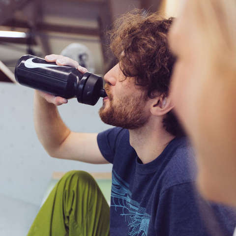Ein Boulderer sitzt in der Boulderhalle auf dem Fussboden und trinkt aus einer schwarzen Trinkflasche.
