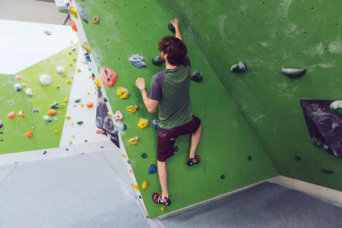 Ein Mann klettert in einer Boulderhalle und demonstriert, wie die Dreipunkt Regel auszuführen ist.