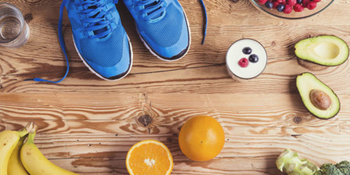 Auf einem Tisch liegen alle möglichen Lebensmittel, die man bei einem Wettkampf zu sich nehmen sollte. Obst, wie Bananan und Orangen und auch Gemüse, wie Avocados und Brokkoli.