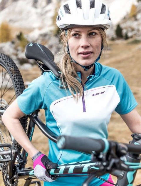 Eine Frau trägt ihr Mountainbike. Sie trägt einen weißen Fahrradhelm von Scott.