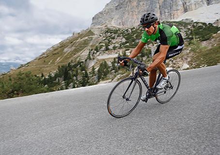 Ein Rennradfahrer ist auf einer Straße unterwegs. Er schützt sich mit einem schwarzen Fahrradhelm.