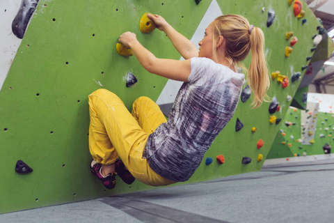 Eine Frau zeigt an einer Boulderwand wie die Stellung von Po zu Wand sein sollte.