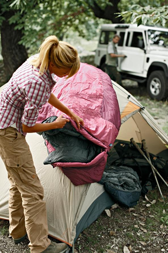 Eine Frau steht vor einem Zelt und packt ihre Sachen w&auml;hrend im Hintergrund ein SUV steht.