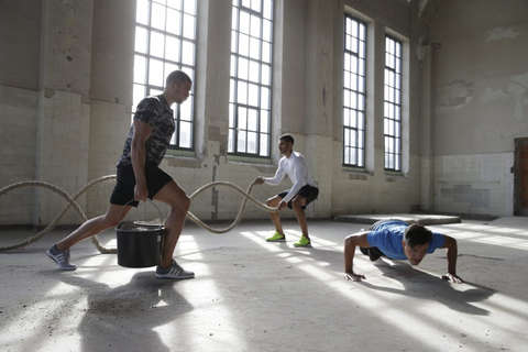 3 Männer beim Functional Training in einer Lagerhalle mit staubigem Fußboden.