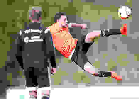 Ein Mann springt beim Fußball in die Luft um den Ball noch zu erwischen.