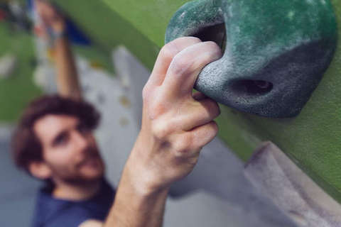 Im Fokus des Bildes ist die Hand eines Boulderers der die Greiftechnik Lochgriff beim klettern verwendet.