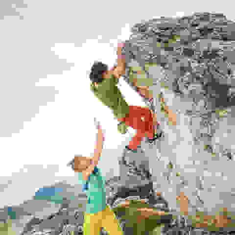Spotten am Fels. Eine Frau sichert einen Kletterer von hinten ab.