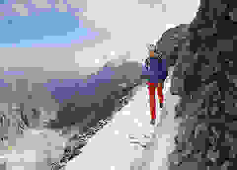 Eine Frau geht einen verschneiten Bergweg entlang.