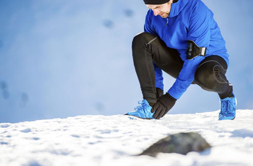 Ein Mann kniet im Schnee und bindet sich die Schuhe.