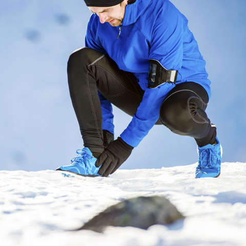 Ein Mann kniet im Schnee und bindet sich die Schuhe.