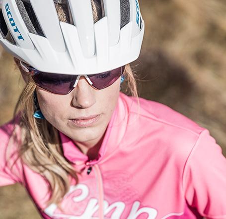 Eine Frau in der Nahaufnahme. Sie trägt eine Sportbrille und einen weißen Fahrradhelm der Marke Scott.