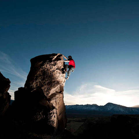 Ein Mann klettert an einem hohen Felsen ohne Sicherung hinauf.