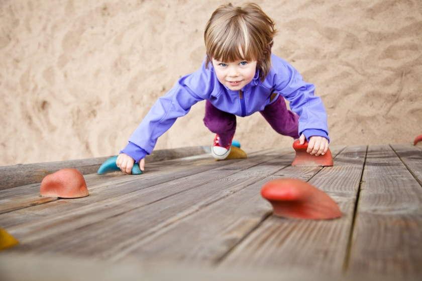 Ein kleines Mädchen klettert im Kinderbereich einer Boulderhalle.