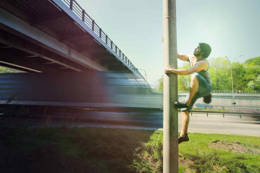 Ein Boulderer klettert einen Betonpfahl hinauf.