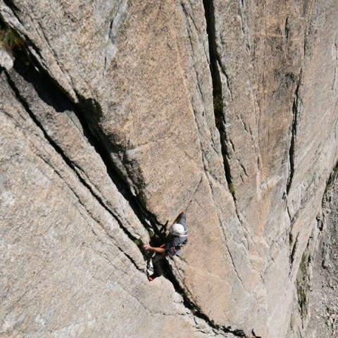 Ein Mann klettert an einer hohen und glatten Felswand an einem schmalen Spalt hinauf. Diese Technik nennt man Rissklettern.