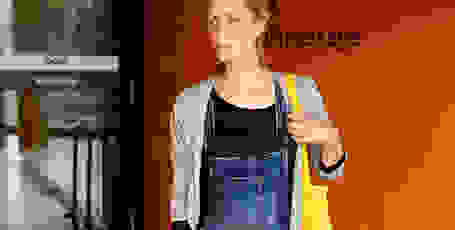 Eine Frau in Jeans Latzhose steht vor dem Eingang einer Einkaufspassage.
