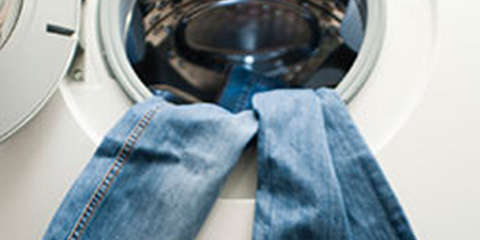 Eine Jeans hängt aus einer Waschmaschine heraus.