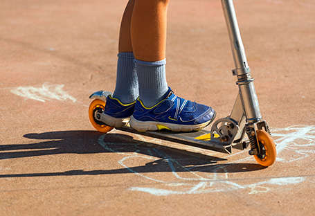 Ein Junge fährt mit Kinder Sneakern auf einem sportlichen Roller.