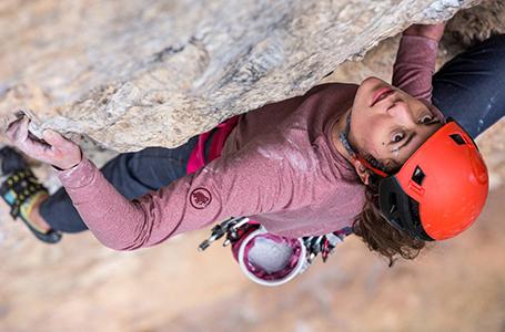 Ein Kletterer hängt an einer Felswand und trägt einen roten Kletterhelm.