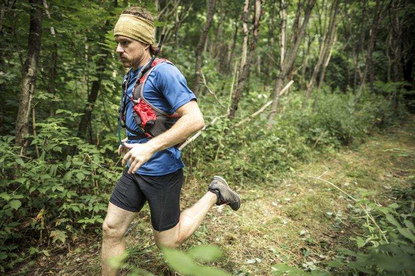 Ein Trailrunner l&auml;uft im Wald. Auf dem Kopf tr&auml;gt er einen Buff.