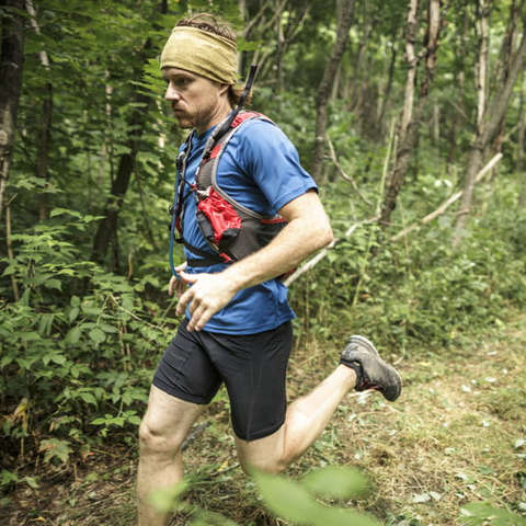 Ein Trailrunner läuft im Wald. Auf dem Kopf trägt er einen Buff.