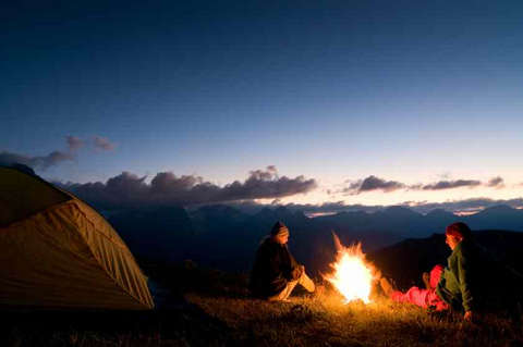 Ein Pärchen sitzt am Abend neben ihrem Zelt am Lagerfeuer.