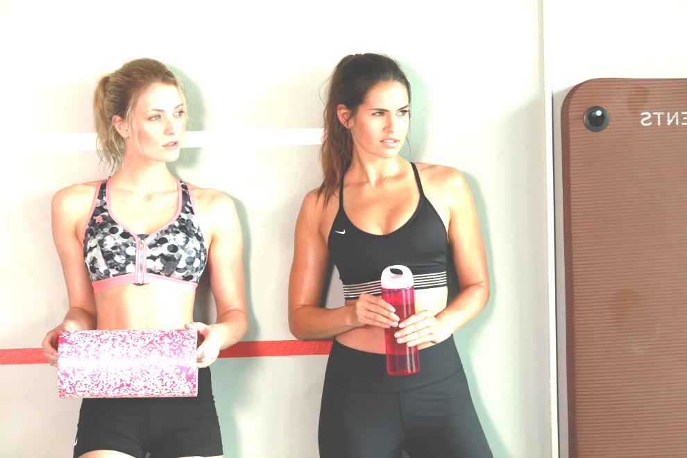 2 Frauen stehen an einer Wand. Eine hält eine große Faszienrolle in der Hand.