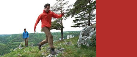 Zwei Männer wandern durch eine grüne Landschaft. Sie tragen dabei Hosen von Maier Sports.