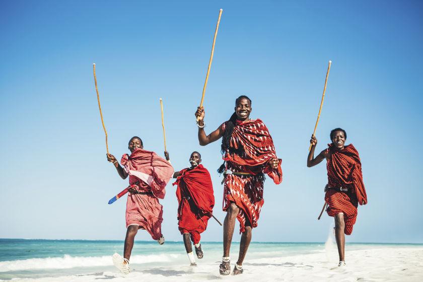 Masai-Kriegerinnen und -Krieger laufen an einem wei&szlig;en Sandstrand