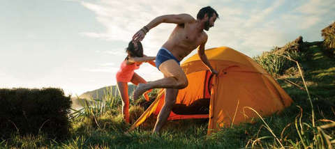 Ein Mann und eine Frau albern um ein Zelt herum. Sie tragen Merino Funktionsunterwäsche.