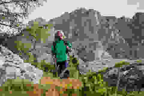 Ein Mann mit langen Haaren wandert mit Wanderstöcken in einem Gebirge.