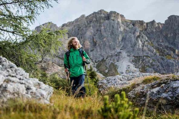 Ein Mann mit langen Haaren wandert mit Wanderst&ouml;cken in einem Gebirge.