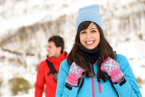 Eine Frau steht in blauer Jacke, mit Mütze und Handschuhen in einer Schneelandschaft.
