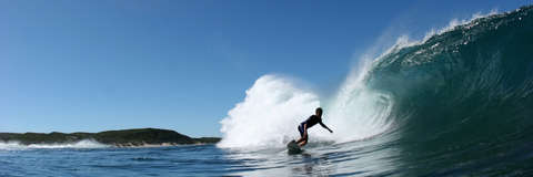 Ein Surfer in Neoprenanzug surft über eine hohe Welle.