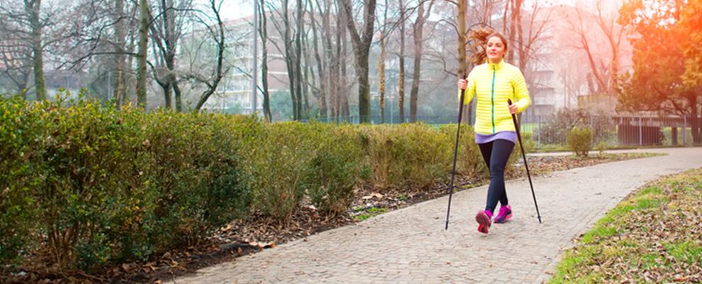 Eine Frau betreibt Nordic Walking in einem Park. Sie geht mit Nordic Walking St&ouml;cken einen Weg entlang.