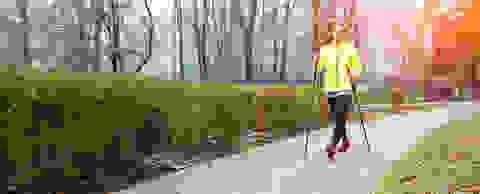 Eine Frau betreibt Nordic Walking in einem Park. Sie geht mit Nordic Walking Stöcken einen Weg entlang.