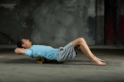 Ein Mann trainiert mit einer Faszienrolle seinen oberen Rücken.