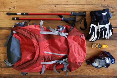 Was steht alles auf deiner Packliste? Ein Rucksack, Handschuhe, Kompass und Sonnenbrille auf einem Holztisch.