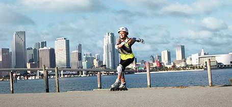 Eine Frau fährt Inline Skates. Sie trägt eine vollständige Schutzausrüstung bestehend aus Knie,-Hand,- und Ellenbogenschonern und auf dem Kopf einen Skatehelm.