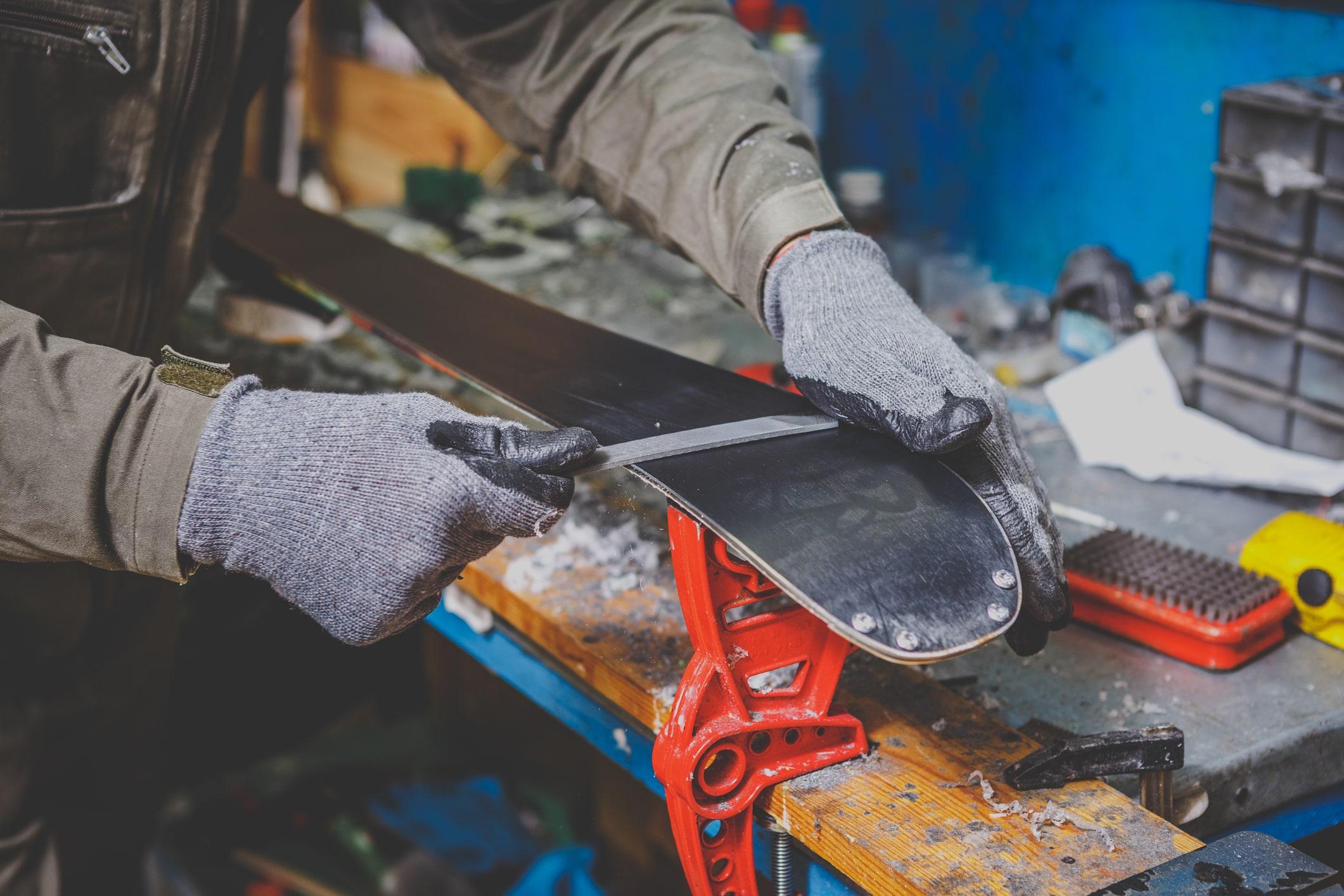 Ein Mann schleift beim Skiservice die kanten eines Skis mit einer Feile